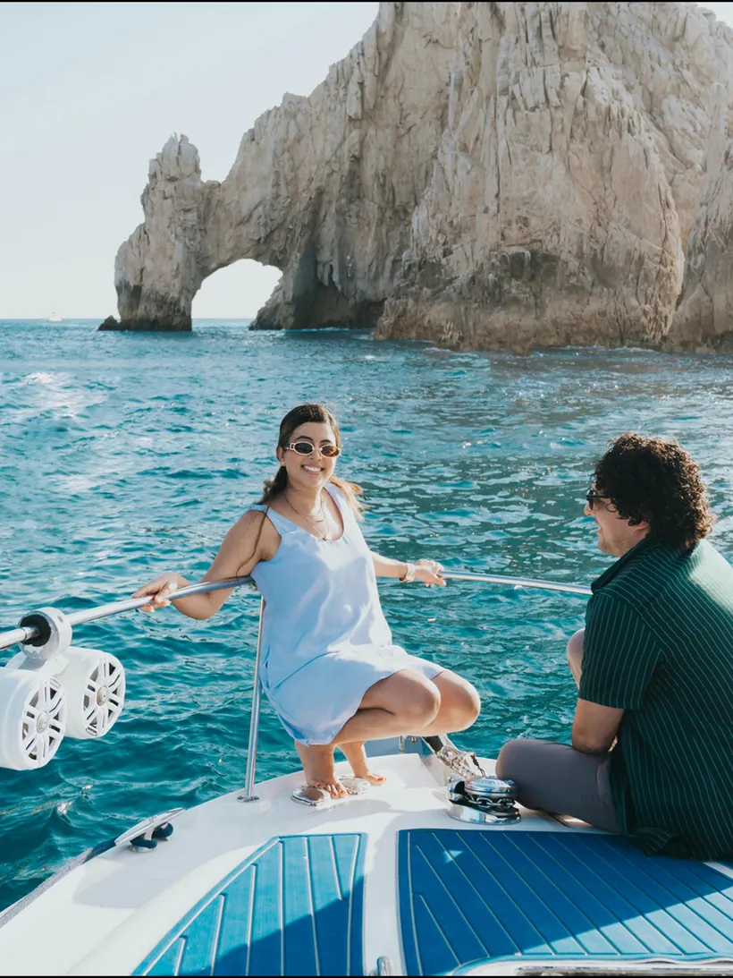 Guests aboard a motor yacht beside a coastal rock arch